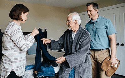 Elderly Patient With Family Members Helping With Clothing