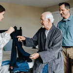 Elderly Patient With Family Members Helping With Clothing